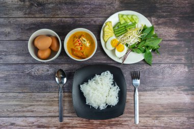 Sebzeli köri soslu Tayland pilavı ve ahşap masada haşlanmış yumurta. Erişte gibi yuvarlak undan yapılmış Tayland yemeği stili, acı biber ezmesiyle yenir..