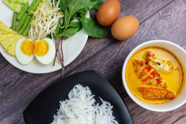 Sebzeli köri soslu Tayland pilavı ve ahşap masada haşlanmış yumurta. Erişte gibi yuvarlak undan yapılmış Tayland yemeği stili, acı biber ezmesiyle yenir..