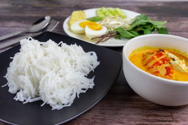 Sebzeli köri soslu Tayland pilavı ve ahşap masada haşlanmış yumurta. Erişte gibi yuvarlak undan yapılmış Tayland yemeği stili, acı biber ezmesiyle yenir..