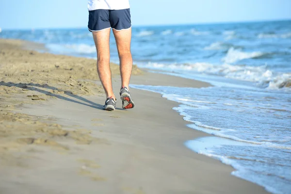 Jambes rapprochées d'un jeune homme courant dans le sable sur le rivage d'une plage au bord de la mer pendant les vacances d'été ensoleillées Images De Stock Libres De Droits