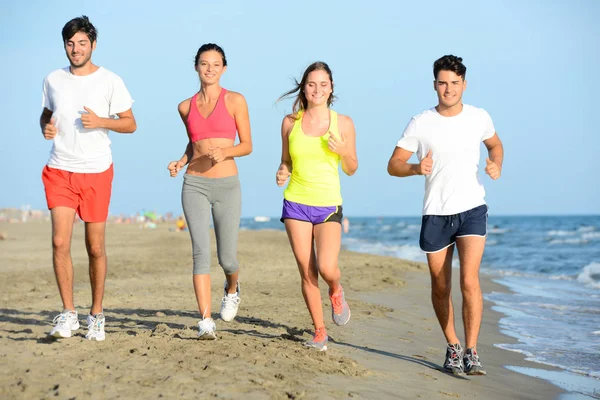 Grupo de jóvenes corriendo en la arena en la orilla de una playa junto al mar al atardecer durante unas vacaciones de verano soleadas Imágenes De Stock Sin Royalties Gratis