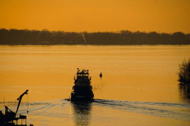 Gün batımında nehirde yüzen bir nehir teknesinin silueti.