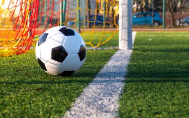 Yüksek açıdan vurulmuş. Top futbol sahasında. Yeşil çimen, beyaz çizgi, futbol kapısından renkli ağ.