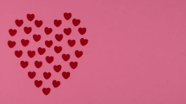 Piccoli cuori rossi che formano la forma di un grande cuore su uno sfondo rosa . — Foto Stock
