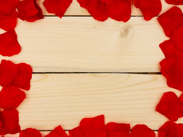 Petali di rosa rossa che formano una cornice su un tavolo di legno . — Foto Stock