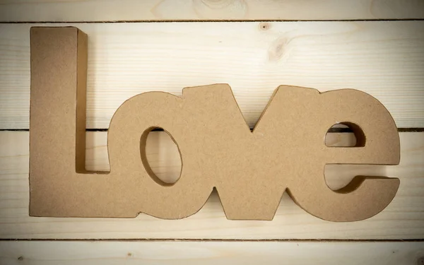 题词"爱"是用纸板制成的，躺在一张木制桌子上. — 图库照片