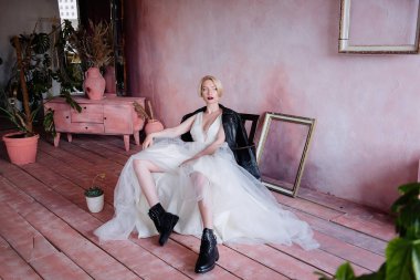 Gelinin olağandışı suretinde güzel bir kız. Narin elbiseli, kaba siyah çizmeli ve siyah deri ceketli gelin..