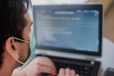 Karantinada uzaktan kumanda. Tüm güvenlik kurallarına uyun. Her yere maske takın. Programcı dizüstü bilgisayara kod yazar.