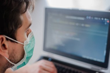 Karantinada uzaktan kumanda. Tüm güvenlik kurallarına uyun. Her yere maske takın. Programcı dizüstü bilgisayara kod yazar.