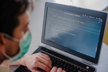 Karantinada uzaktan kumanda. Tüm güvenlik kurallarına uyun. Her yere maske takın. Programcı dizüstü bilgisayara kod yazar.