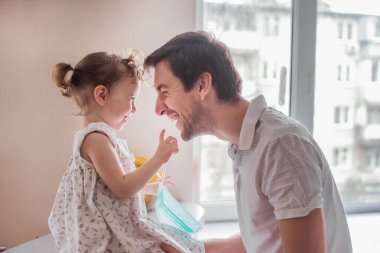 Küçük kız babasına tıbbi maske takıyor. Ailede birbirimize değer veriyoruz. Karantinada yaşam.