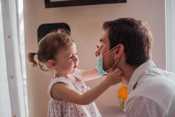 Küçük kız babasına tıbbi maske takıyor. Ailede birbirimize değer veriyoruz. Karantinada yaşam.