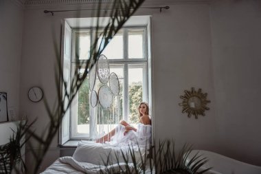 Gelin büyük pencerede damadı bekliyor. Beyaz, uzun elbiseli, çekici bir gelin..