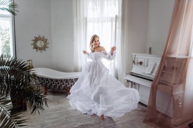 Uzun beyaz elbiseli güzel bir gelin odada daireler çiziyor. Her kız için önemli bir gün. Bir gelinin modern görüntüsü..