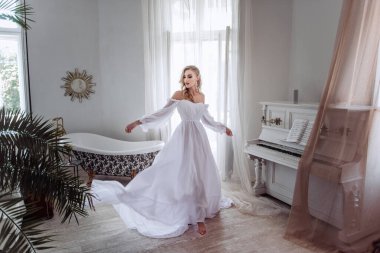 Uzun beyaz elbiseli güzel bir gelin odada daireler çiziyor. Her kız için önemli bir gün. Bir gelinin modern görüntüsü..