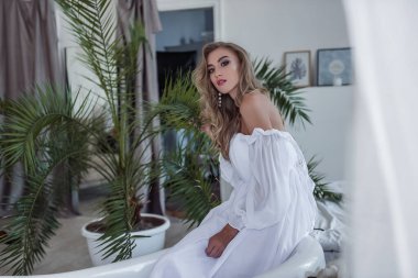 Gelinin narin, havadar ve modern görüntüsü. Açık renkli ve güzel beyaz elbiseli güzel bir kız elinde alışılmadık bir çiçek tutuyor. Modern bir gelin için alışılmadık bir buket. Seçici Odaklanma