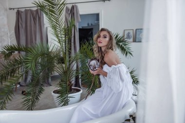 Gelinin narin, havadar ve modern görüntüsü. Açık renkli ve güzel beyaz elbiseli güzel bir kız elinde alışılmadık bir çiçek tutuyor. Modern bir gelin için alışılmadık bir buket. Seçici Odaklanma