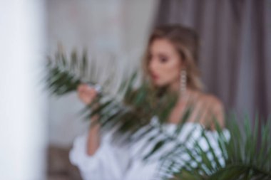 Gelinin narin, havadar ve modern görüntüsü. Açık renkli ve güzel beyaz elbiseli güzel bir kız elinde alışılmadık bir çiçek tutuyor. Modern bir gelin için alışılmadık bir buket. Seçici Odaklanma