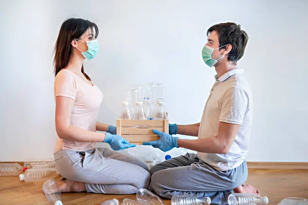 Sorting trash in quarantine and self-containment. A guy and a girl in medical masks are putting empty plastic bottles in boxes. It is very important today to sort the garbage at present.
