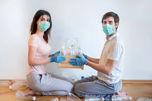 Sorting trash in quarantine and self-containment. A guy and a girl in medical masks are putting empty plastic bottles in boxes. It is very important today to sort the garbage at present.