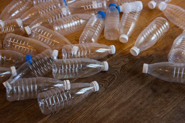 Ahşap zeminde, beyaz ve mavi kapaklı dağınık plastik şişeler. Atık ayıklama ve temizleme, plastiği durdurun. Çevre kirliliğini durdurun. Dünyayı çöplerden korumam gerek.