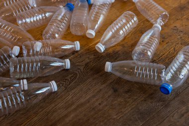 Ahşap zeminde, beyaz ve mavi kapaklı dağınık plastik şişeler. Atık ayıklama ve temizleme, plastiği durdurun. Çevre kirliliğini durdurun. Dünyayı çöplerden korumam gerek.