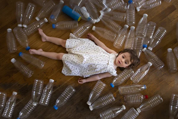 A little girl lies among a huge number of empty bottles. With plastic, we poison not only the environment, but also ourselves, children. Sorting and recycling eco plastic.