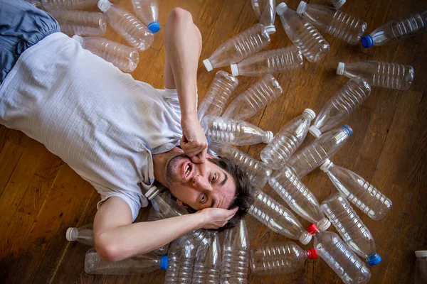 A man lies among environmental plastic bottles. We and our surrounding plastic world. Keep the planet clean, sort and recycle the garbage and plastic.