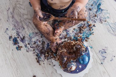 Güzel bir çocuk ilk pastasını mahveder, ayaklarını yalar ve mavi krem içinde yuvarlanır - bebek hayatının ilk doğum günü, Seçici ve Arka Ön Odaklanma
