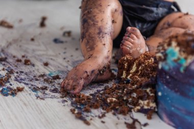 Güzel bir çocuk ilk pastasını mahveder, ayaklarını yalar ve mavi krem içinde yuvarlanır - bebek hayatının ilk doğum günü, Seçici ve Arka Ön Odaklanma