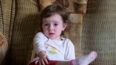 Küçük kız videoya çekildiği için kızgın - çocuk akıllı telefondan oyalanmaktan hoşlanmıyor, kaşlarını çatıyor ve hayal kırıklığına uğruyor. Bebeğin elinde bir cep telefonu var ve kırmızı pantolon giyiyor.