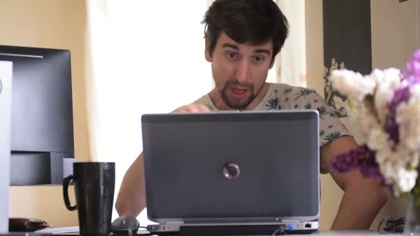 Mladý muž blogger s vousy a rozcuchané vlasy se baví živě a streamuje na notebooku, aktivně gestikuluje rukama, směje se, dává prezentaci, černý šálek stojí vedle notebooku