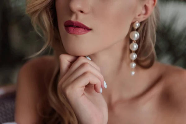 A beautiful girl with natural, beautiful, professional makeup and a fancy fashion fashion cut in her hair and long white pearl earrings. hands near the face, a large portrait. selective focus