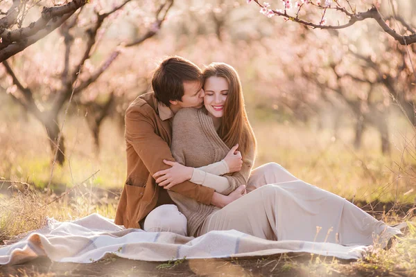 一个穿着棕色浅色夹克的年轻人轻轻地拥抱着一个后面留着长发的漂亮女孩 一对夫妇在一个开花的花园里自然地坐着 有选择地前后聚焦 — 图库照片