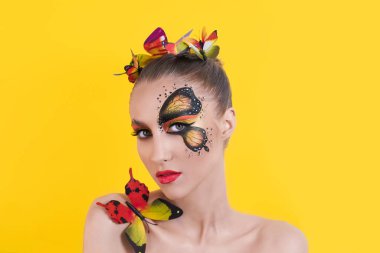 Sarı üniformalı güzel bir kız modelinin yakın plan portresi. Gözünde turuncu bir kelebek resmi, dudaklarında kırmızı ruj, topuz şeklinde sarı saçlar.. 