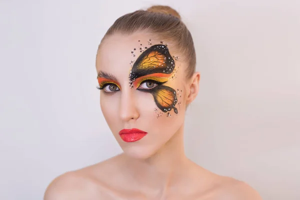 Beyaz üniformalı güzel bir kız modelinin yakın plan portresi. Gözünde turuncu bir kelebek şekli, dudaklarında kırmızı ruj, topuz şeklinde sarı saçlar..
