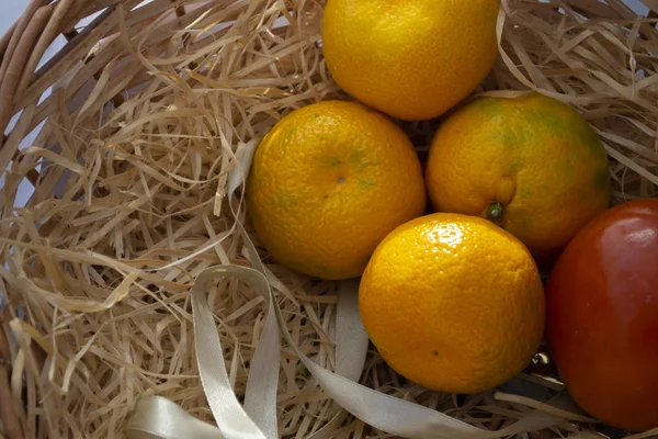 Fruit in a basket on a light background. Apple, mandarin, persimmon in a goat on a light background.