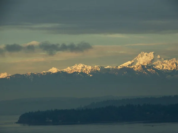Puget Sound 'daki Point Jefferson' ı destekleyen Olympic Mountain Range 'da, Seattle yakınlarındaki Shoreline, Washington' daki Richmond Plajı 'ndan alınan karlı Kardeşler Tepeleri de dahil..