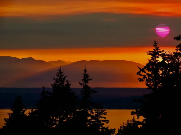 Washington, Kingston yakınlarındaki Puget Sound ve Olympic Mountain tepelerindeki orman yangınlarından çıkan dumanlar yüzünden turuncu gün batımında pembe güneş..