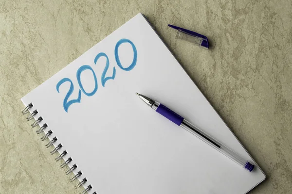 白色笔记本和蓝色题词2020 蓝笔在纸上 帽子在桌子上 — 图库照片