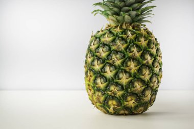 Olgun bir ananas açık gri arkaplanlı beyaz bir yüzeyde durur..