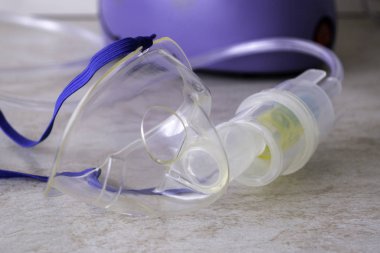Tedavi amaçlı buhar solumak için bir cihaz. İlaç için maske ve matara. Arka planda da astım spreyinin bir kısmı var..