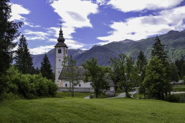 Dağ gölünün kıyısındaki eski taş kilise. Yeşil dağ sırası ve beyaz bulutlu mavi gökyüzü.