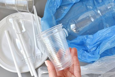 Plastik bardakları tutan kadın, sofra takımı, şişeler, arka planda torbalar, plastik atık konsepti.