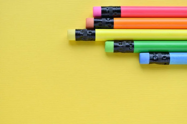 Pencils with erasers in rainbow colors on textured yellow paper, top view, copy space. Arts, back to school background.