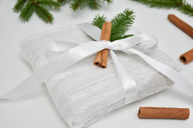 Beyaz kumaş ve kurdeleyle paketlenmiş yaratıcı Noel hediyesi, süslenmiş köknar dalı ve tarçın çubuğu.