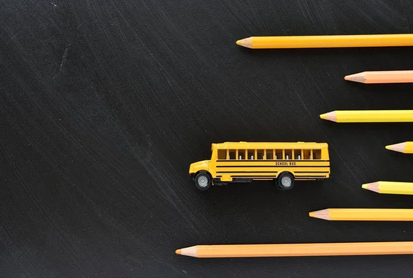 Back to school concept, education, yellow school bus and pencils on black chalkboard, copy space.