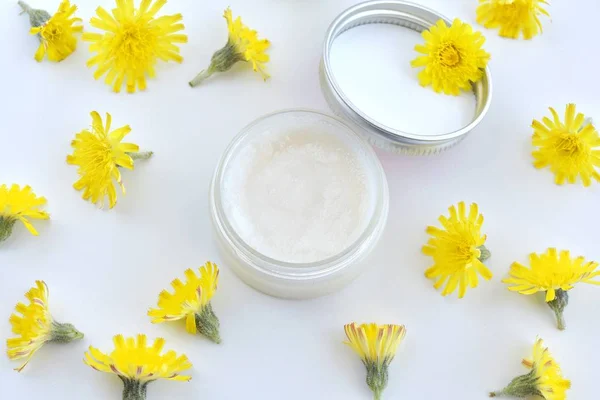 Natural, organic, homemade lip balm in small container, handmade cosmetic, flat lay with yellow flowers.