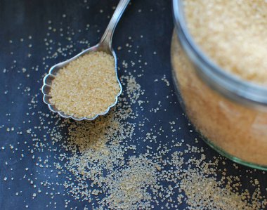 Esmer kamış şekeri eski kaşık ile kavanozda. Koyu arkaplanda yakın plan görünümü.