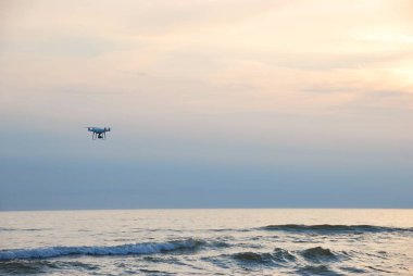 Drone akşam gökyüzünde denizin üzerinde uçuyor.